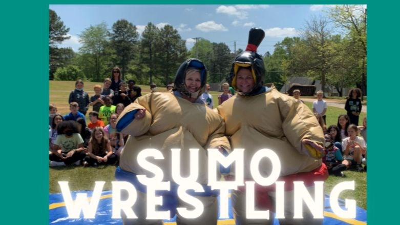 Sumo wrestling - picture of two women in sumo wrestling suits with happy students in the background